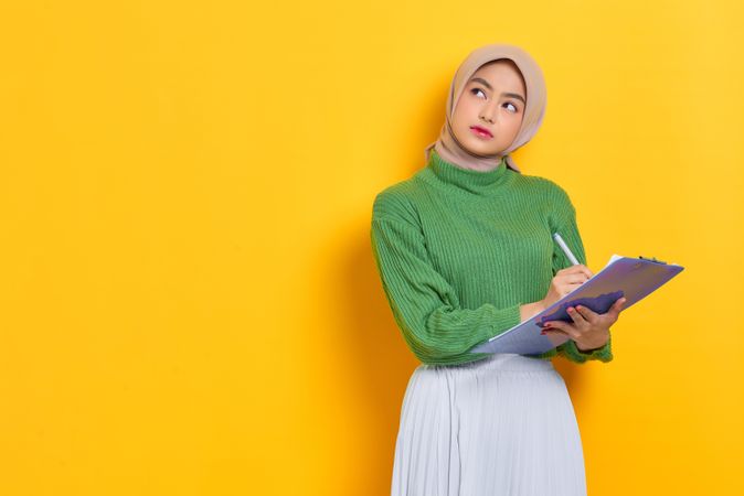 Woman in headscarf holding clipboard looking up while thinking about something