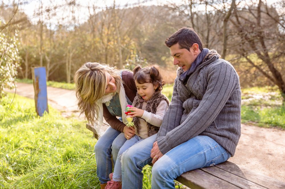 Parents with small girl with drink on park bench in forest