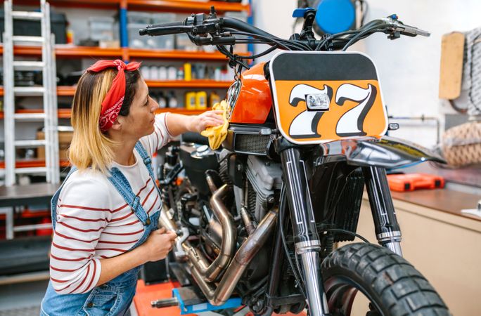 Mechanic woman cleaning motorcycle with cloth and polish on factory
