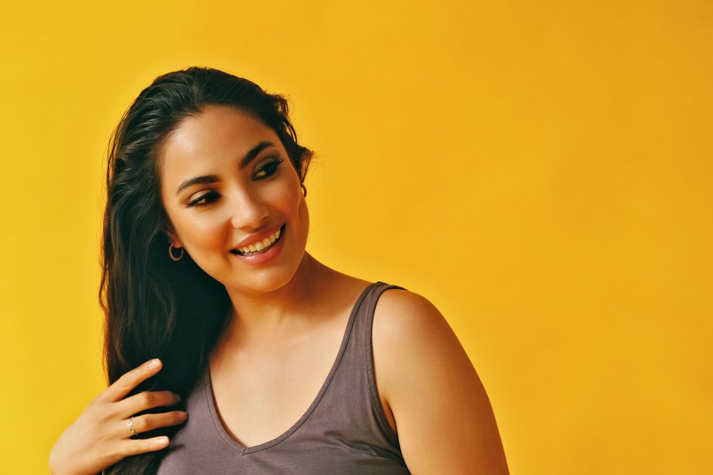 Headshot of Hispanic woman with head tilted to side on yellow background