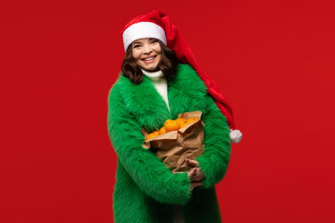 Woman in Santa hat holds paper bag of oranges.