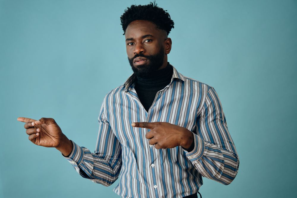 Serious Black man in striped shirt pointing to the side with both hands