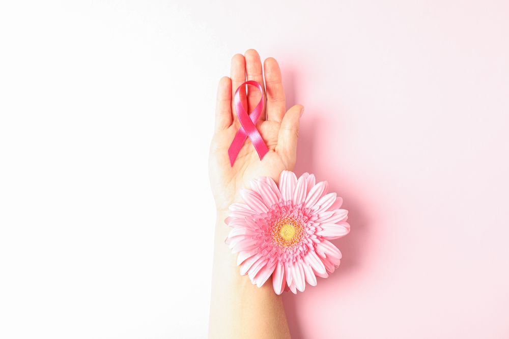 Female hand with pink awareness ribbon and gerbera color background