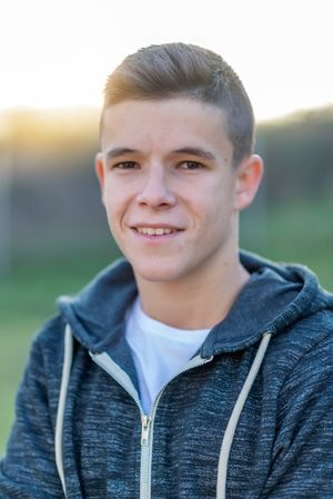 Teenage male in hoodie standing in field smiling at camera