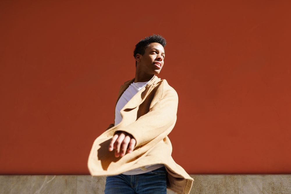Black male in camel coat with hand towards camera