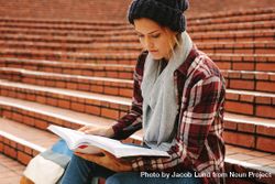 Young woman reading book on university stairs bYdG14