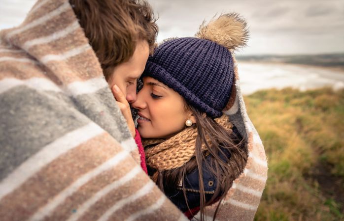 Close up of tender moment between a couple while wrapped in blanket on a windy day