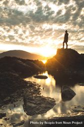 Silhouette of person standing on rock formation near body of water during sunset 0J6rd0