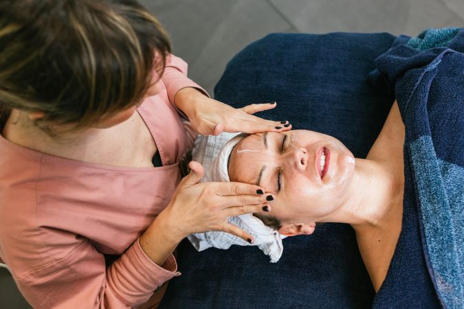 Crop beautician cleansing face of woman in salon