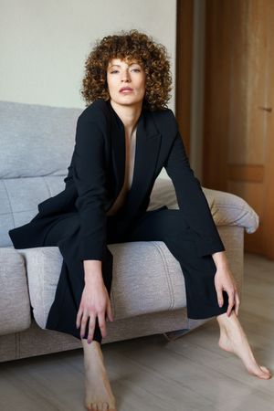 Woman in dark suit sitting forward on sofa at home