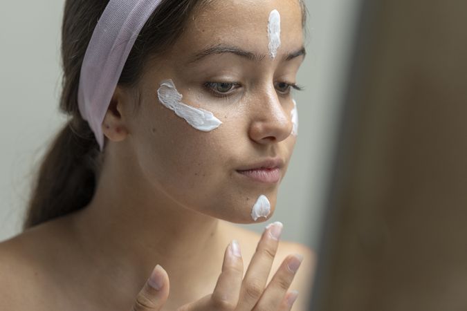 Young woman applying dots of face cream or foundation before blending, skincare routine