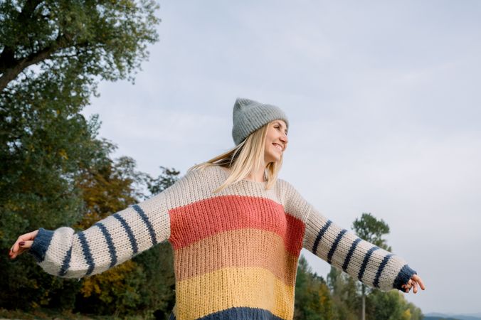Happy woman with arms outstretched wearing knitwear and hat