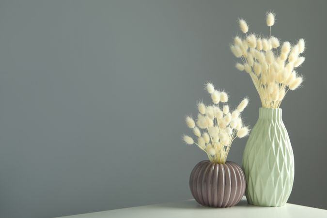 Textured round vase and tall vase filled on table with dried grass in grey room with copy space