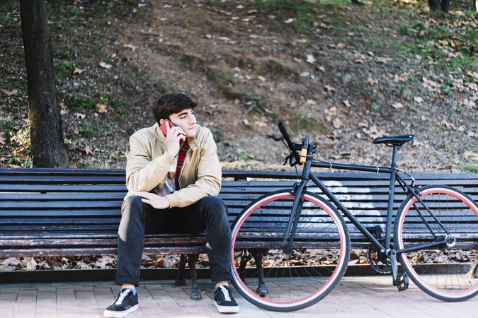 Man sitting on bench outside next to bike talking on phone