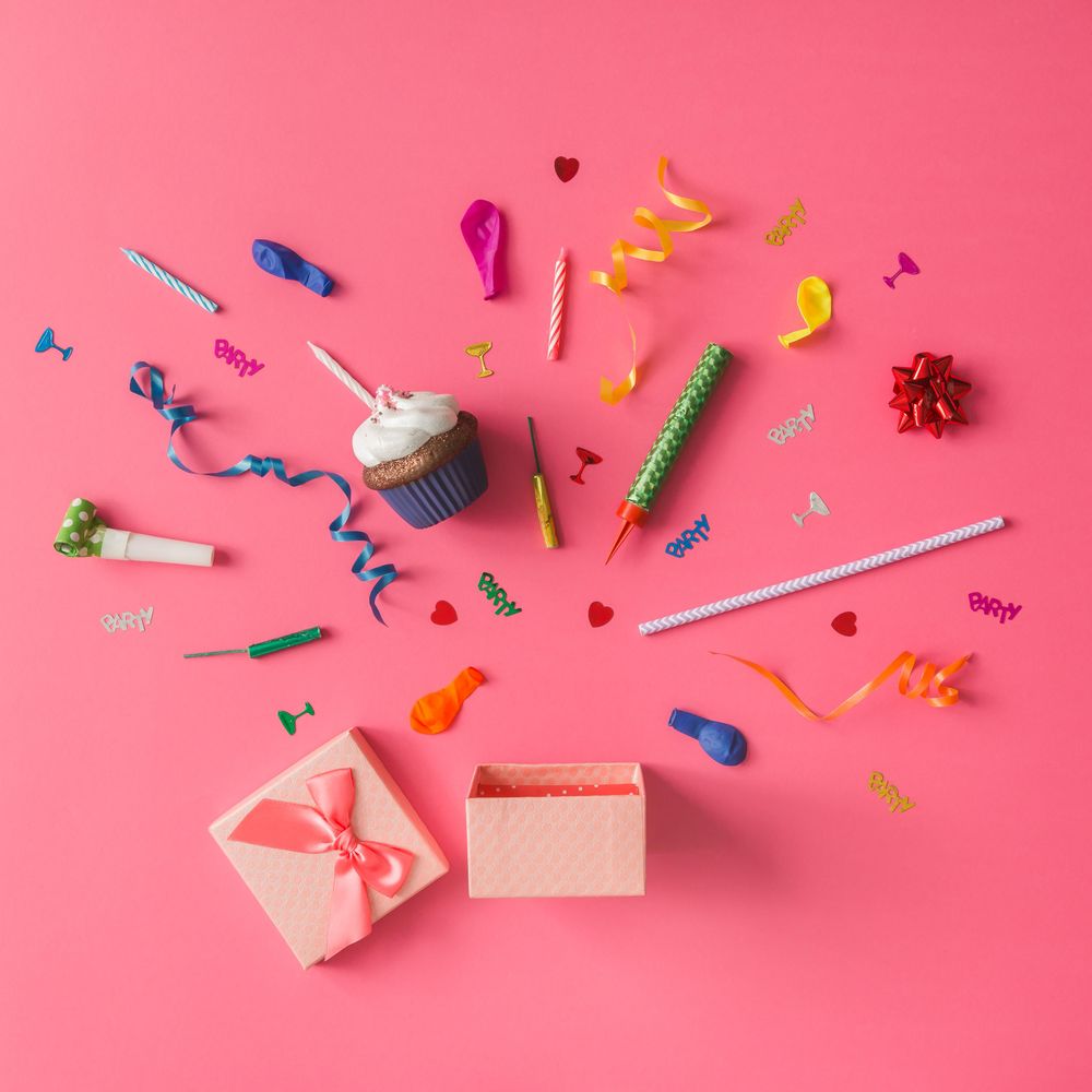 Gift box with colorful party items on pink background
