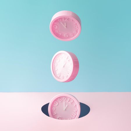 Pastel pink clocks on blue and pink backdrop falling into a hole