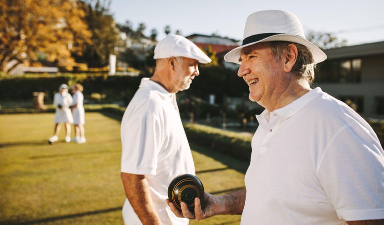 Older men in hats playing boules on a lawn with friends