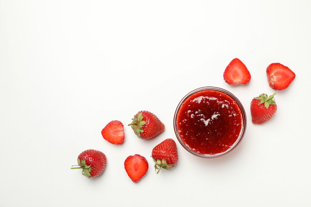 Strawberry and bowl with jam on plain background, space for text