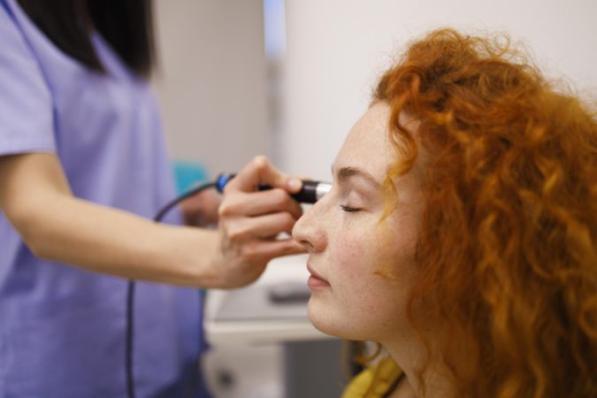 Red haired woman in clinic with medical device to her eye