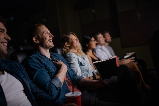 Group of friends sitting in multiplex movie theater with popcorn and drinks
