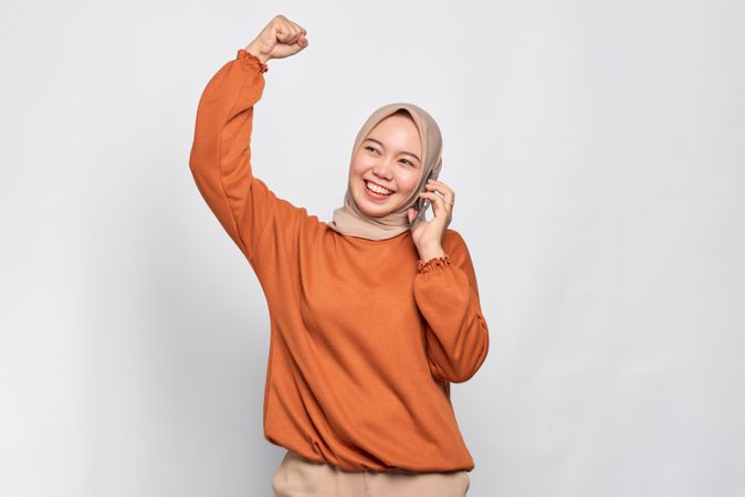 Muslim woman celebrating something with smart phone to her ear