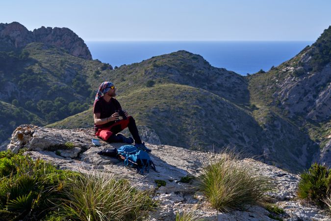Male traveler sitting on mountain slope with binoculars