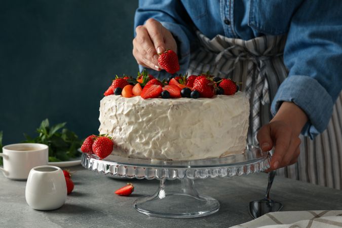 Woman puts strawberry on berry cream cake. Delicious dessert