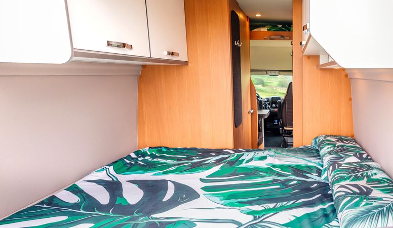 Bed with green linen inside of empty motorhome
