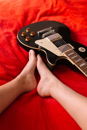 Crop female musician with electric guitar on bed