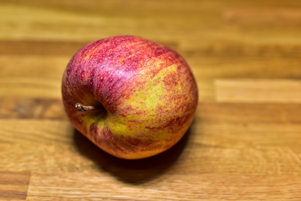 A crisp, red apple sits enticingly on a rustic wooden table