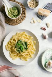Served plate of pesto pasta next to bowl of sauce on table