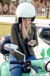 Woman in helmet sitting on bike and looking to mobile phone