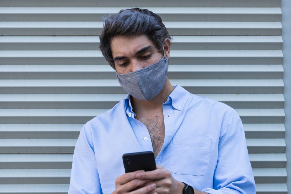 Man in mask browsing smartphone on street