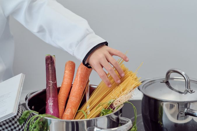 Crop preteen boy adding spaghetti into saucepan while preparing