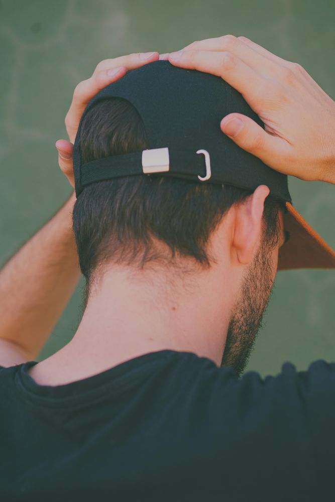 Back view of man with dark cap touching his head
