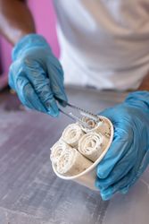 A worker is putting chocolate ice cream rolls in a tub using tongs and latex gloves