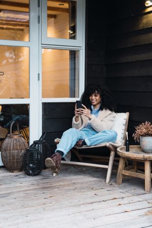 Cheerful Black woman browsing smartphone on terrace