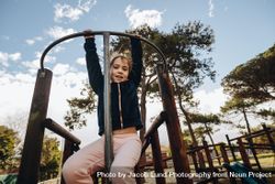 Portrait of young girl hanging on a climbing frame by her arms bYX3G4