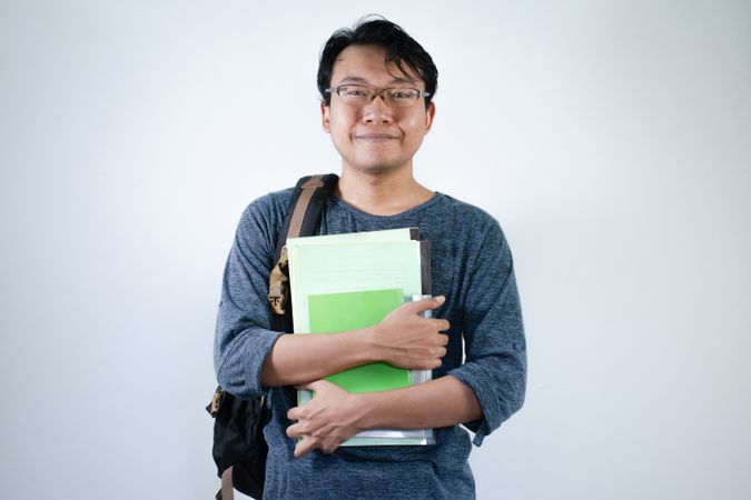 Asian young male student wearing bag and carrying books smiling and happy expression