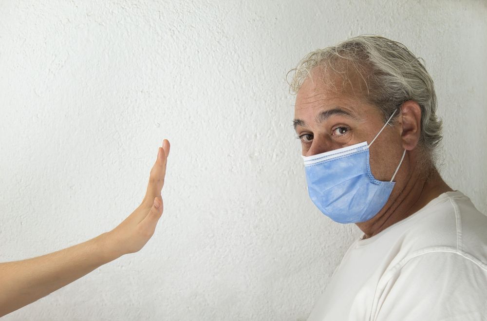 Side view of middle aged man with facemask being stopped by a hand