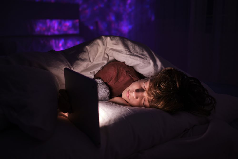 Boy sleeping near tablet in bed at night