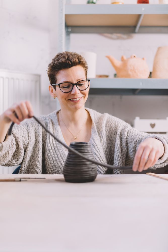 Adult woman putting clay roll on unfinished pot