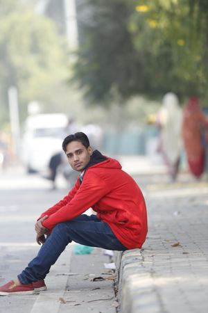 Man in red hoodie sitting on sidewalk