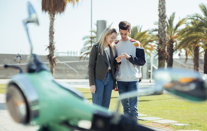 Woman and man standing and looking at mobile phone near too bike