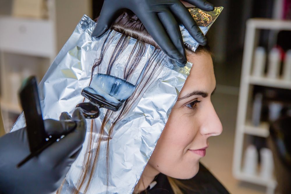 Closeup of hairdresser hands applying hair dye to client with brush