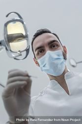 Low angle view of male dentist in medical mask holding dentist tools for dental procedure in clinic 5Xz8vb