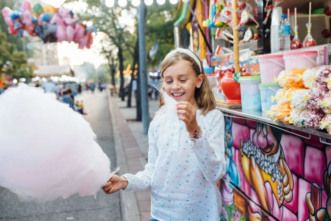 Cheerful girl eating cotton candy on street