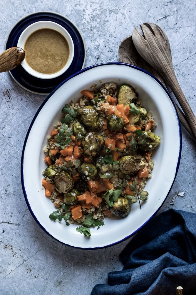 Braised brussels sprouts and pumpkin with quinoa in bowl near cup of sauce