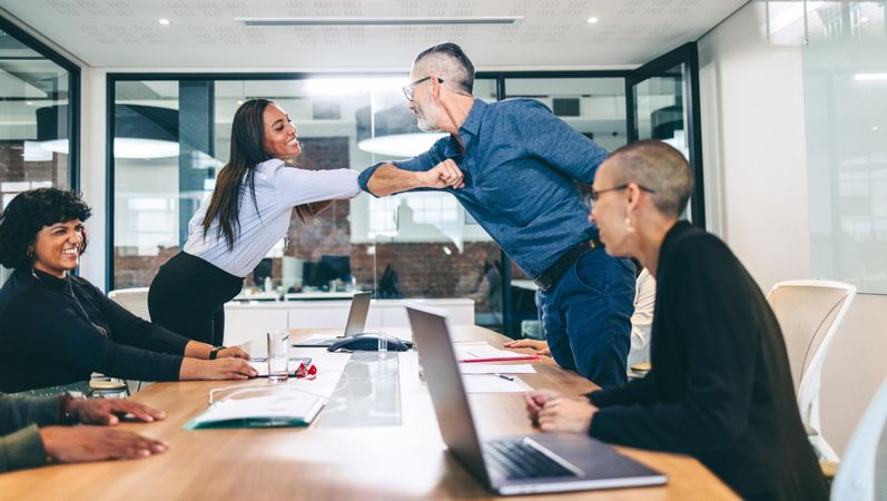 Happy businesspeople elbow bumping each other before a meeting in a boardroom