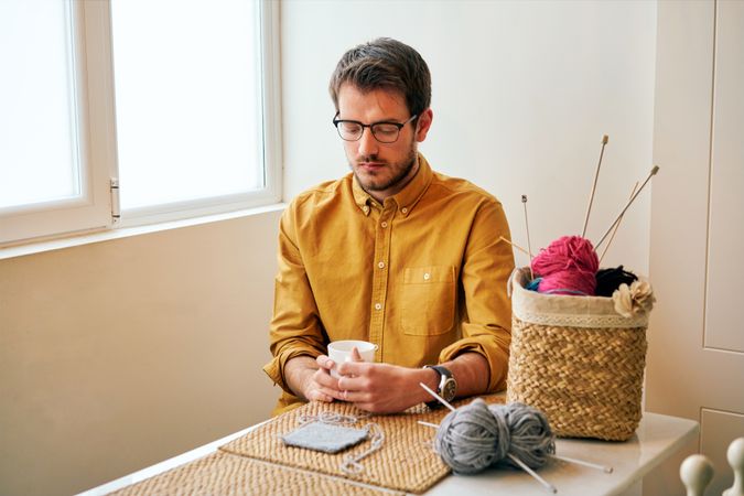 Man drinking hot tea during knitting